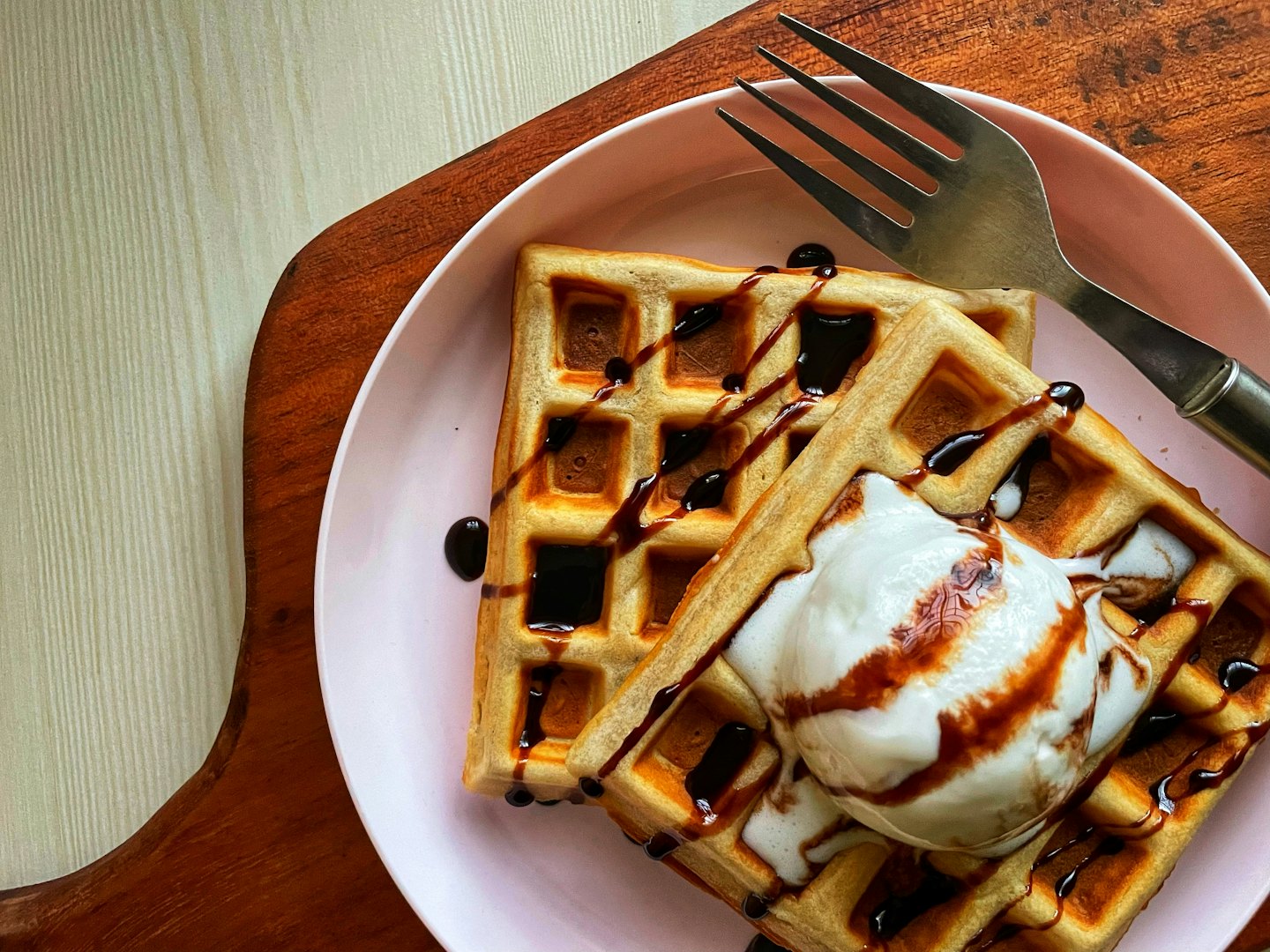 Two golden waffles topped with melting ice cream and chocolate sauce.