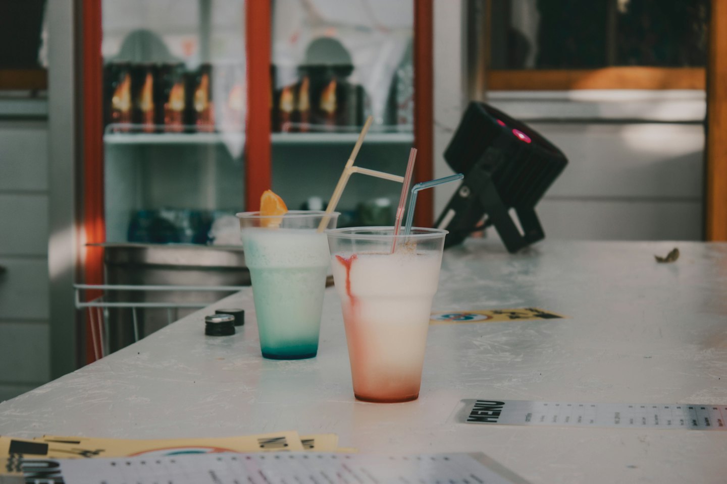 Two colorful frozen drinks with fruit garnishes on a white table.