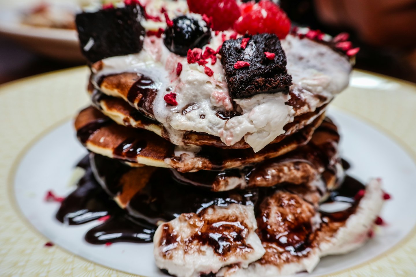 Stack of pancakes topped with fruit, brownie pieces, and cream.