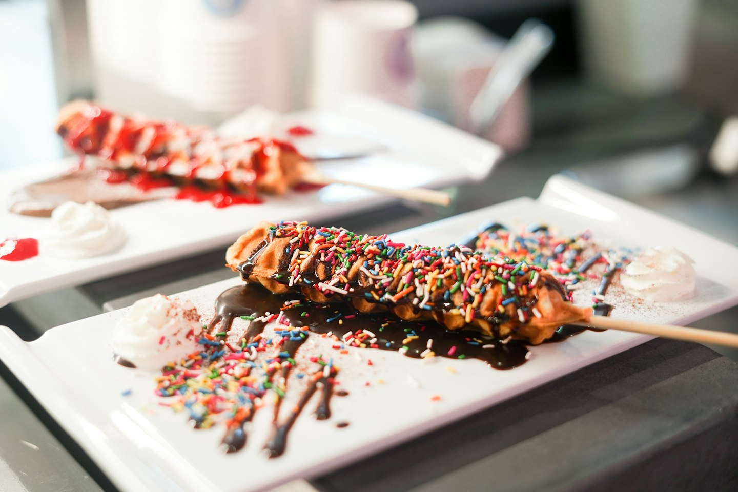 Two decorative waffles on sticks topped with syrup and cream.