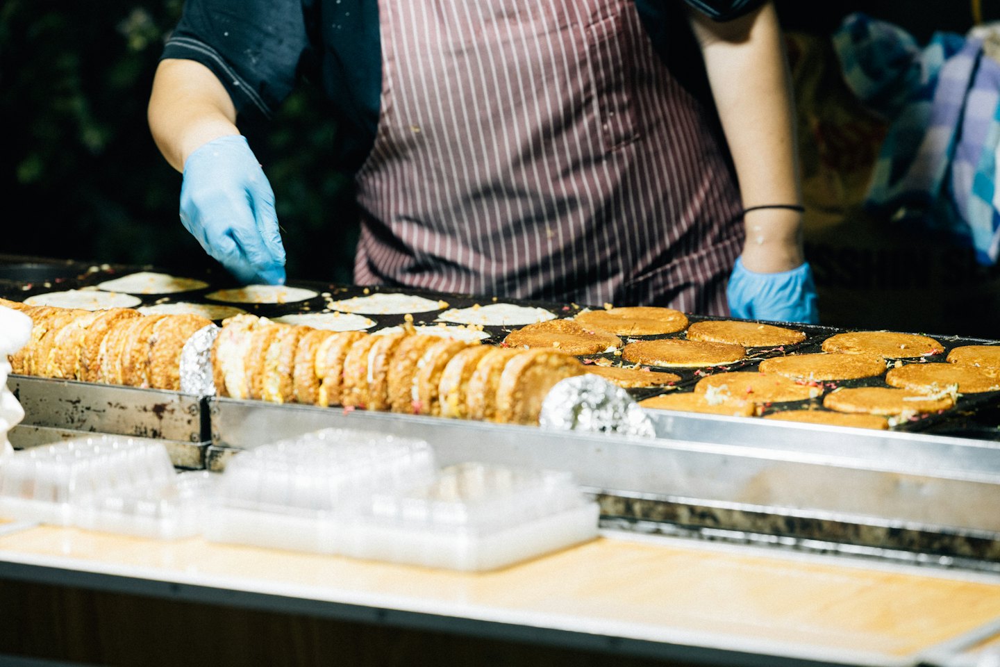 Vendor in blue gloves cooks round pancakes on a griddle.