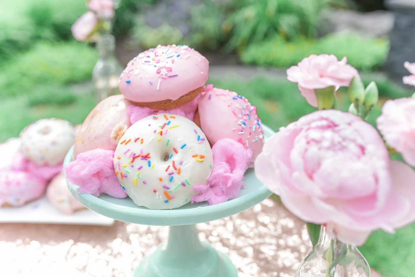 Pink and white donuts with sprinkles on a cake stand with flowers.