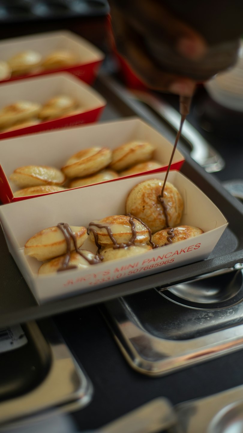 Mini pancakes drizzled with chocolate syrup in white trays.