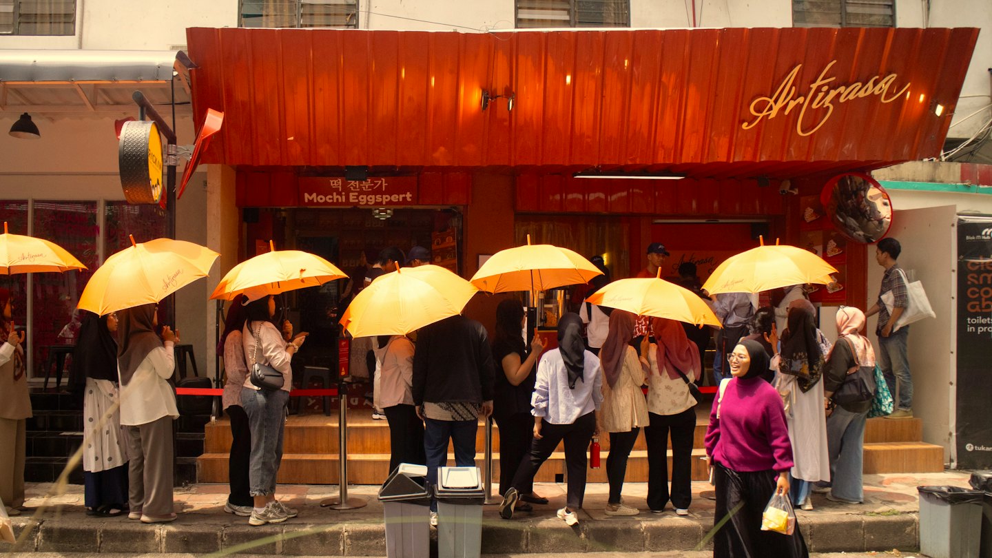 Customers with orange umbrellas wait in line outside a dessert shop.