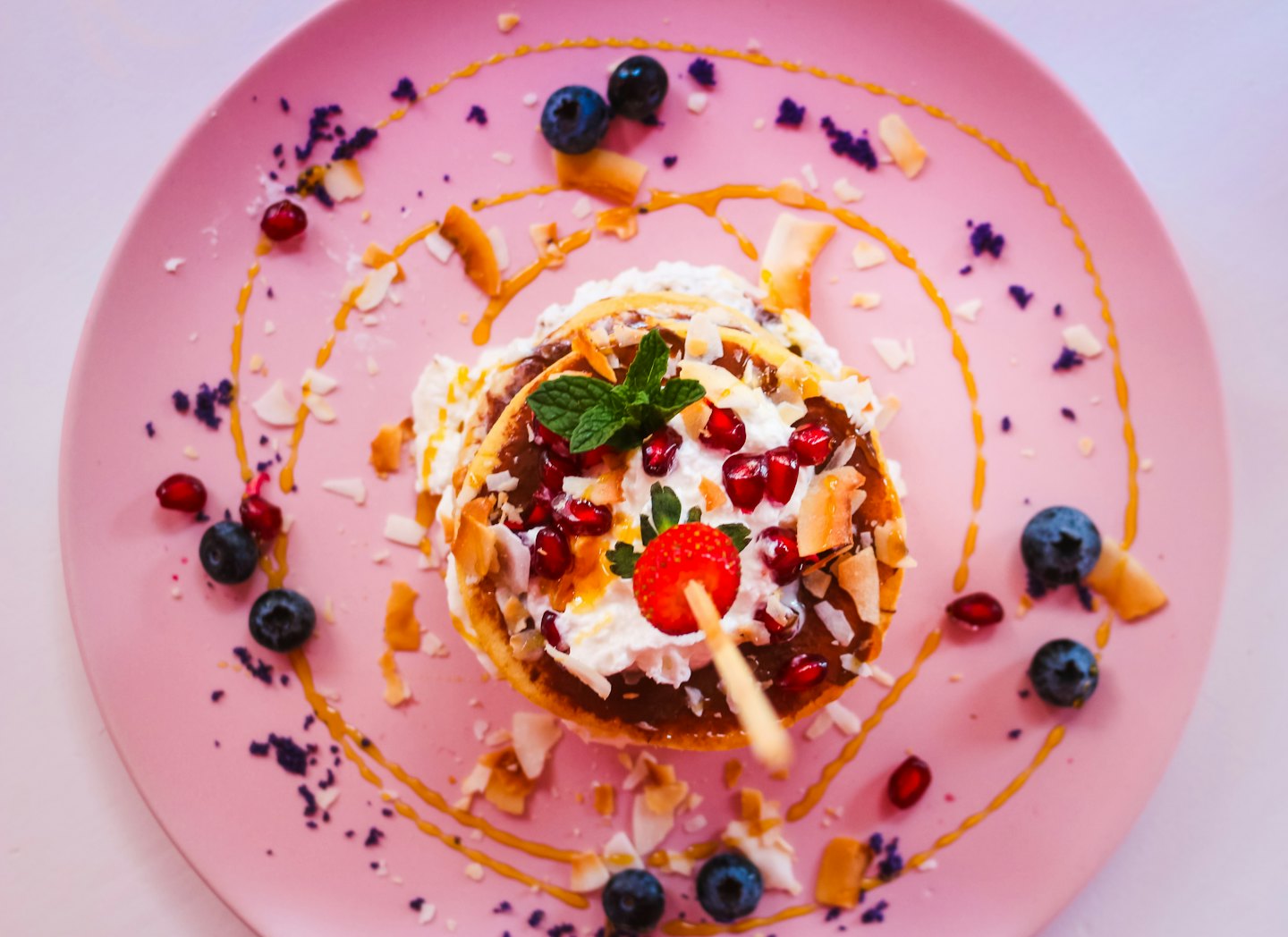 Stack of pancakes topped with fruit and syrup on a plate.
